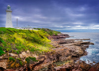Green Cape Lighthouse, Beowa National Park NSW — the white tower and keepers' cottages above a green headland, red rock ledges and the sea
