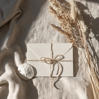 Sapphire Coast Photography gift card — cream envelope tied with twine on linen with a sand dollar and dried coastal grasses