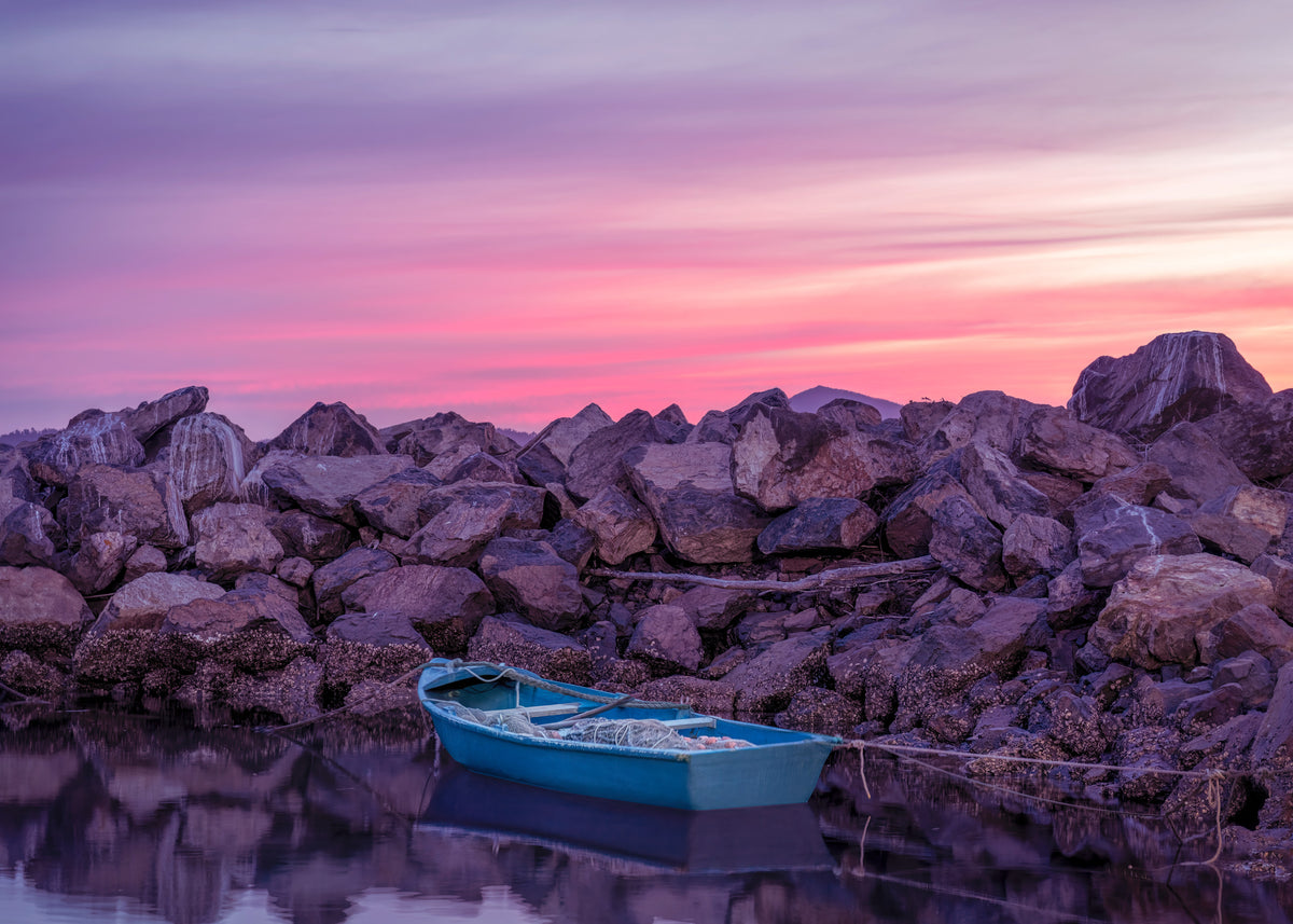 Twofold Hush, Eden NSW — small blue dinghy against the breakwall rocks under a pink and violet sky, Twofold Bay