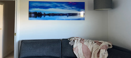 Dawn Delight Merimbula Lake panorama acrylic hanging above a grey sofa in a customer's lounge room